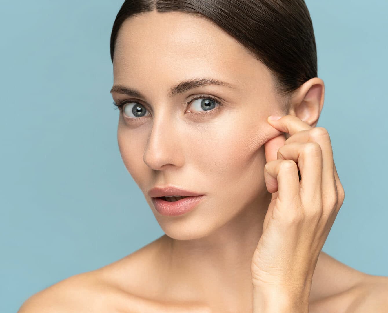 Woman with smooth, healthy skin gently touching her jawline against a soft blue background